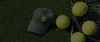 Dark green custom logo cap next to tennis balls and a racquet, custom team merch from Connie's Impressions in Hammond, LA
